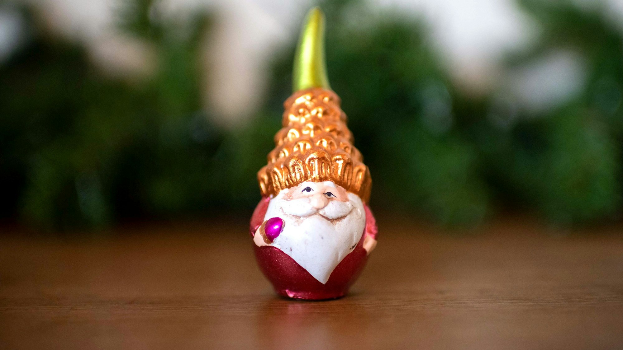 Eine Weihnachtsmannfigur steht auf einem Tisch, im Hintergrund sind Tannenzweige zu erkennen.