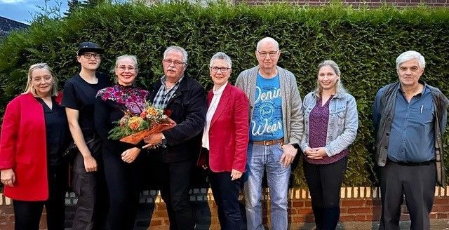 Männer und Frauen stehen nebeneinander. Einer hält einen Blumenstrauß.