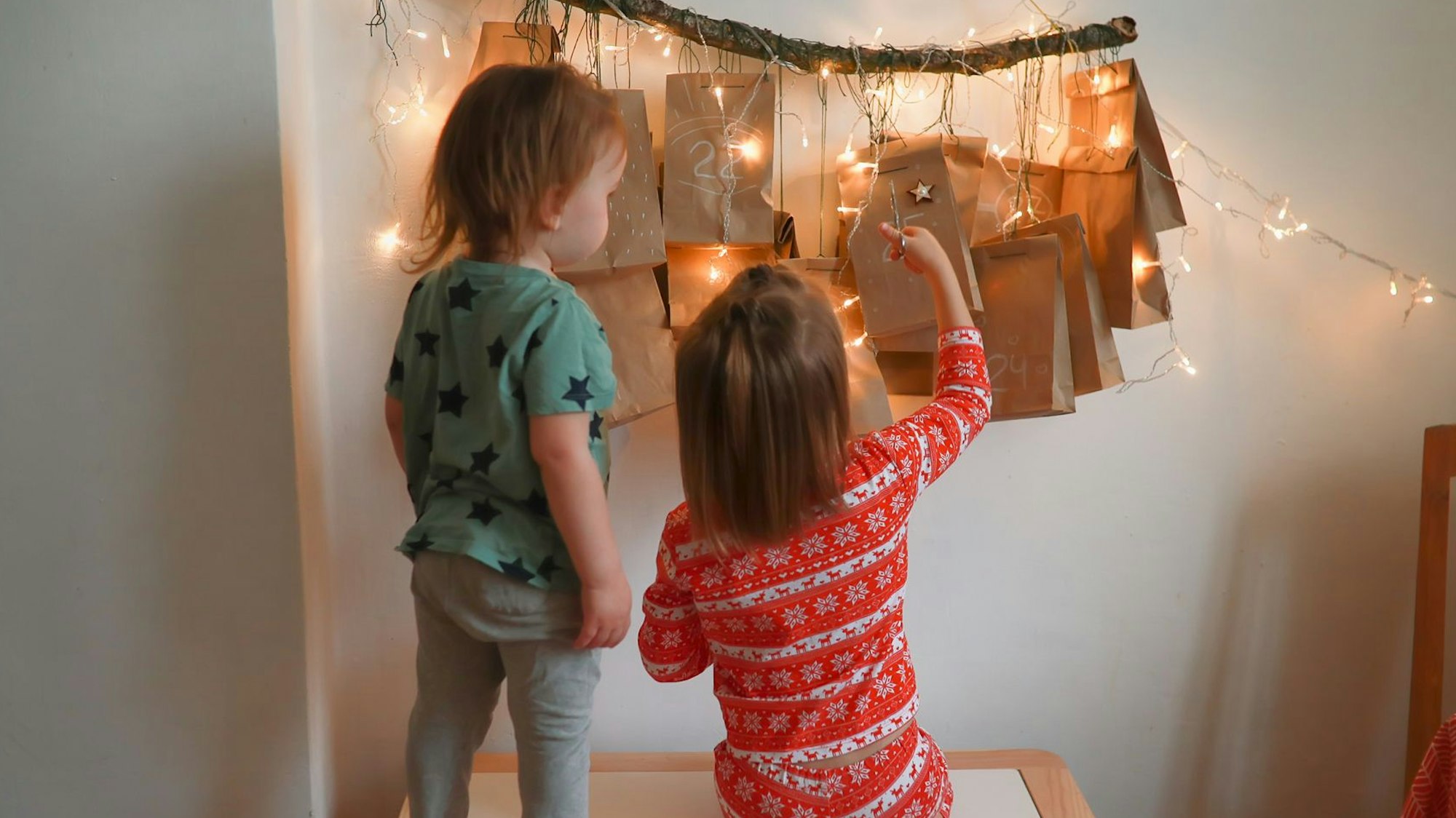 Zwei kleine Kinder stehen vor einem erleuchteten Adventskalender.