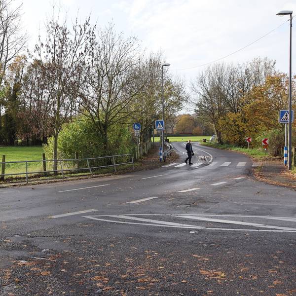 Die Einmündung auf eine von Wiesen gesäumte Straße ist zu sehen.