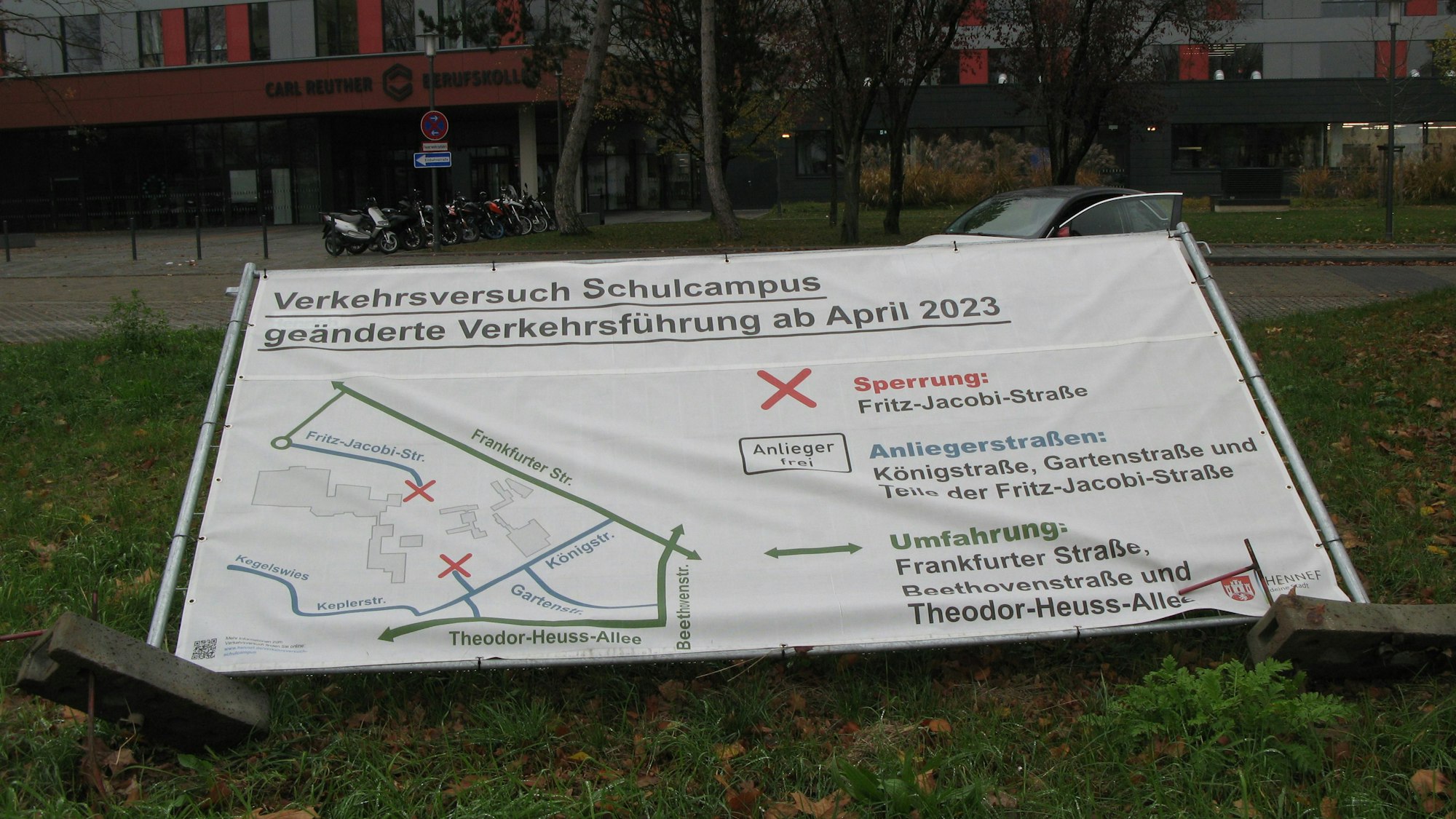 Ein Into-Transparent zum Verkehrsversuch „Autofreier Schulcampus“ ist umgekippt und liegt im Gras.