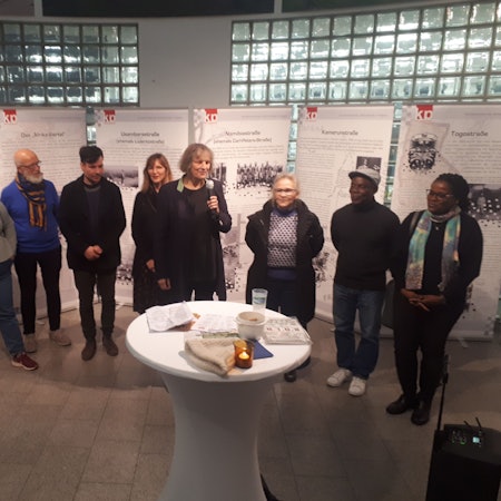 Vor Aufstellwänden stehen etwa zehn Menschen. Eine Dame hält ein Mikrofon in der Hand.