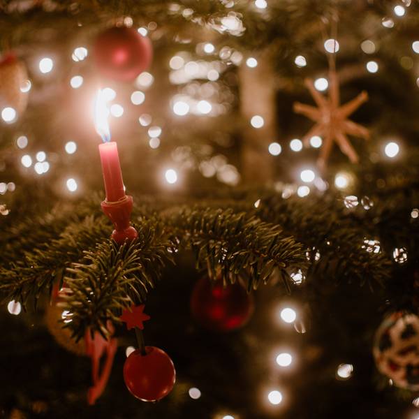 Nahaufnahme einer Kerze an einem Weihnachtsbaum, der mit einer Lichterkette geschmückt ist