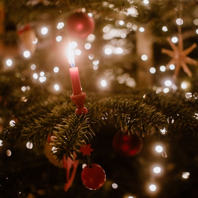 Nahaufnahme einer Kerze an einem Weihnachtsbaum, der mit einer Lichterkette geschmückt ist