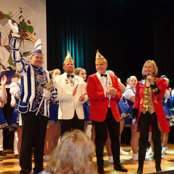 Auf einer Bühne stehen Mitglieder einer Karnevalsgesellschaft. In ihrer Mitte steht der Prinz und winkt ins Publikum.
