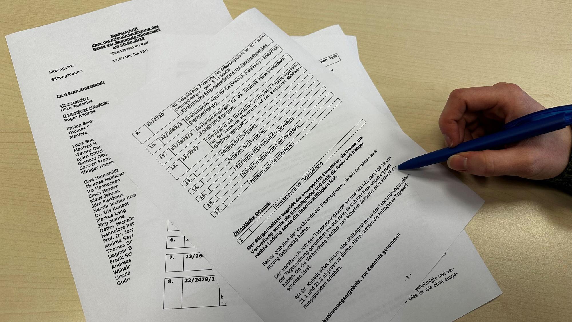 Mehrere Blätter Papier mit Informationen zu Tagesordnungspunkten einer politischen Sitzung liegen auf einem Tisch. Eine Frau markiert mit einem Kugelschreiber eine Textpassage.