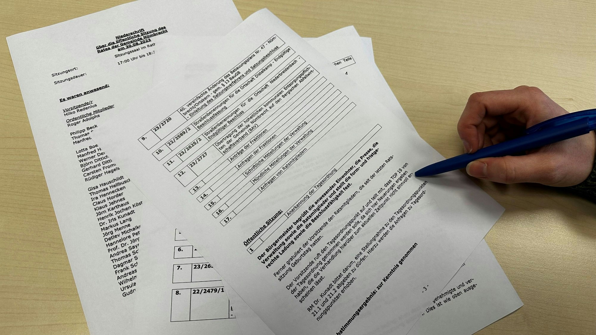 Mehrere Blätter Papier mit Informationen zu Tagesordnungspunkten einer politischen Sitzung liegen auf einem Tisch. Eine Frau markiert mit einem Kugelschreiber eine Textpassage.