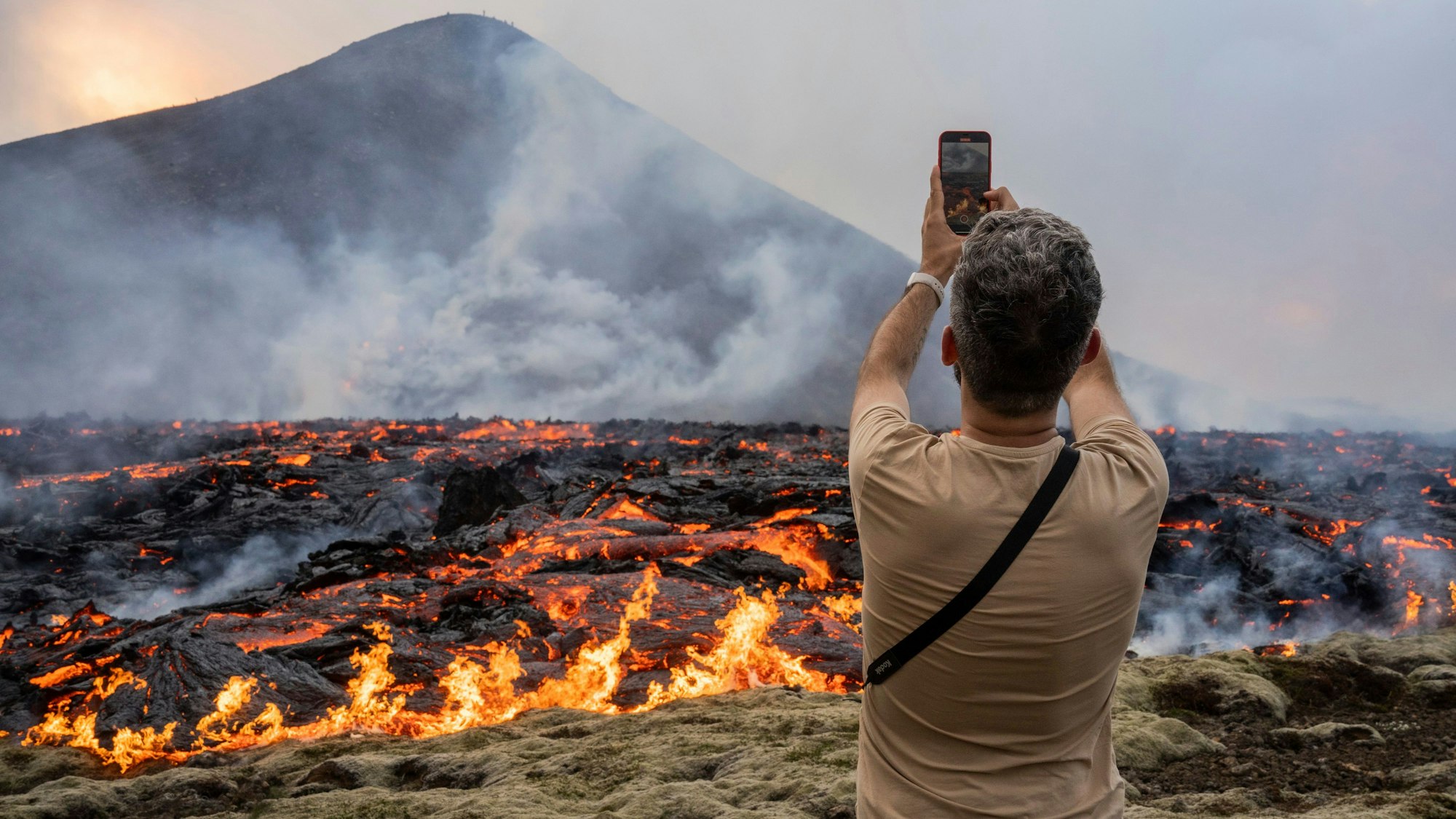 10.07.2023, Island, Fagradalsfjall: Ein Mann fotografiert, wie Lava aus einer Spalte eines Vulkans in der Nähe des Berges Litli-Hrútur, etwa 30 Kilometer südwestlich von Reykjavik, austritt. Auf Island ist es im dritten Jahr in Folge zu einem vulkanischen Ausbruch gekommen. Störungen des Flugverkehrs seien nicht zu befürchten, teilte die isländische Regierung mit. Foto: Marco Di Marco/AP/dpa +++ dpa-Bildfunk +++