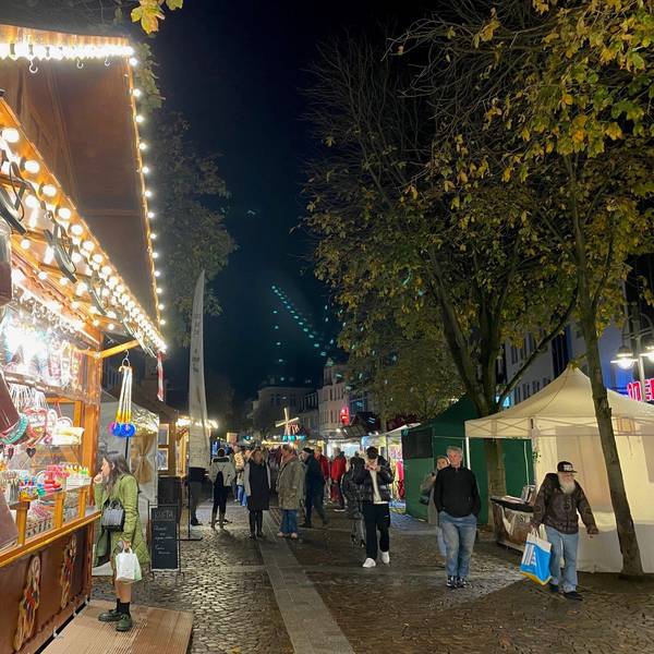 Zu sehen sind Menschen vor bunt erleuchteten Ständen in der historischen Brühler Innenstadt.