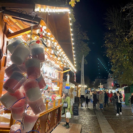 Zu sehen sind Menschen vor bunt erleuchteten Ständen in der historischen Brühler Innenstadt.