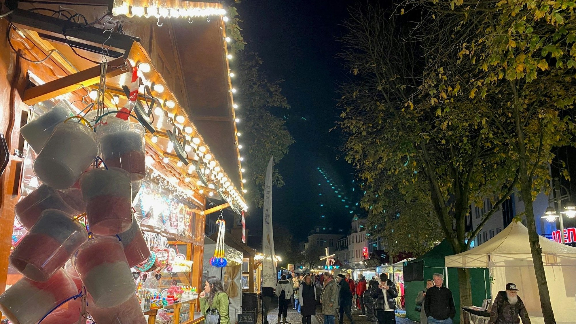 Zu sehen sind Menschen vor bunt erleuchteten Ständen in der historischen Brühler Innenstadt.