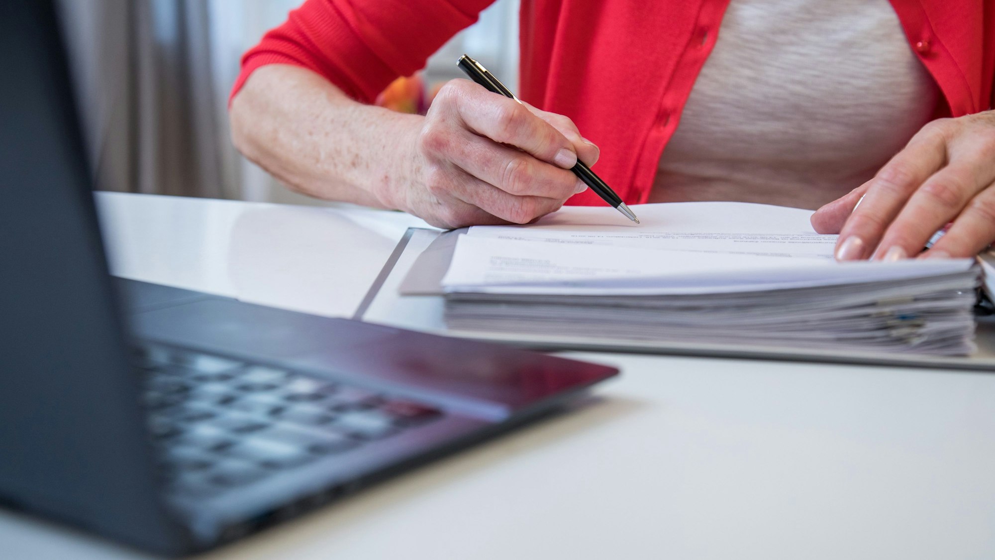 Eine ältere Frau sitzt vor einem Laptop und füllt Formulare aus.