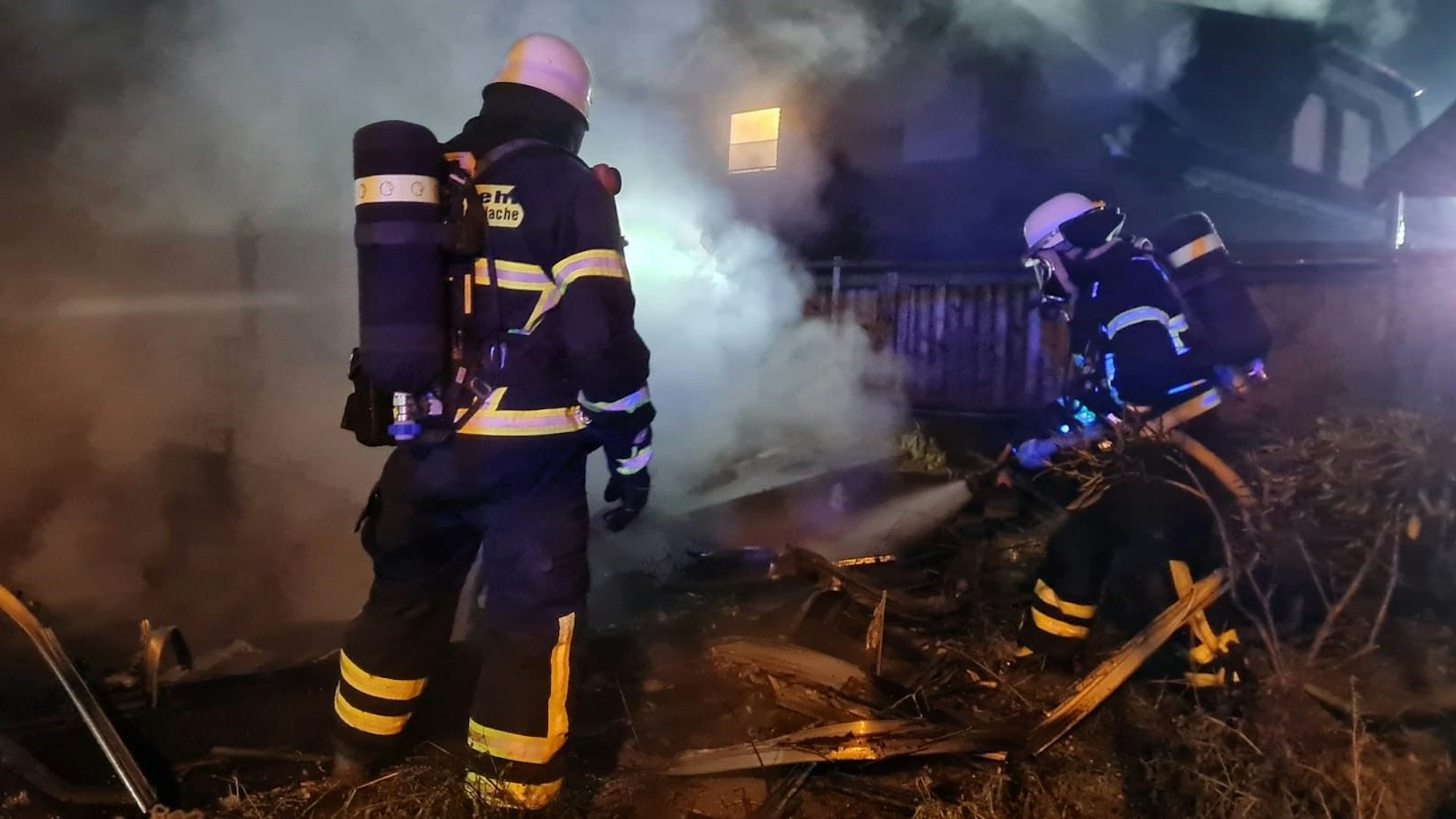 Das Bild zeigt zwei Feuerwehrleute, wie sie dabei sind, den Brand des Gewächshauses zu löschen.