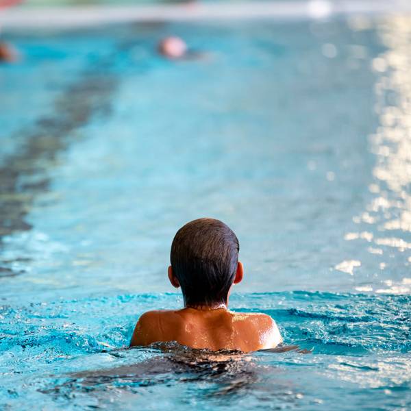 Eine Person, die von Hinten zu sehen ist, schwimmt in einem Hallenbecken.