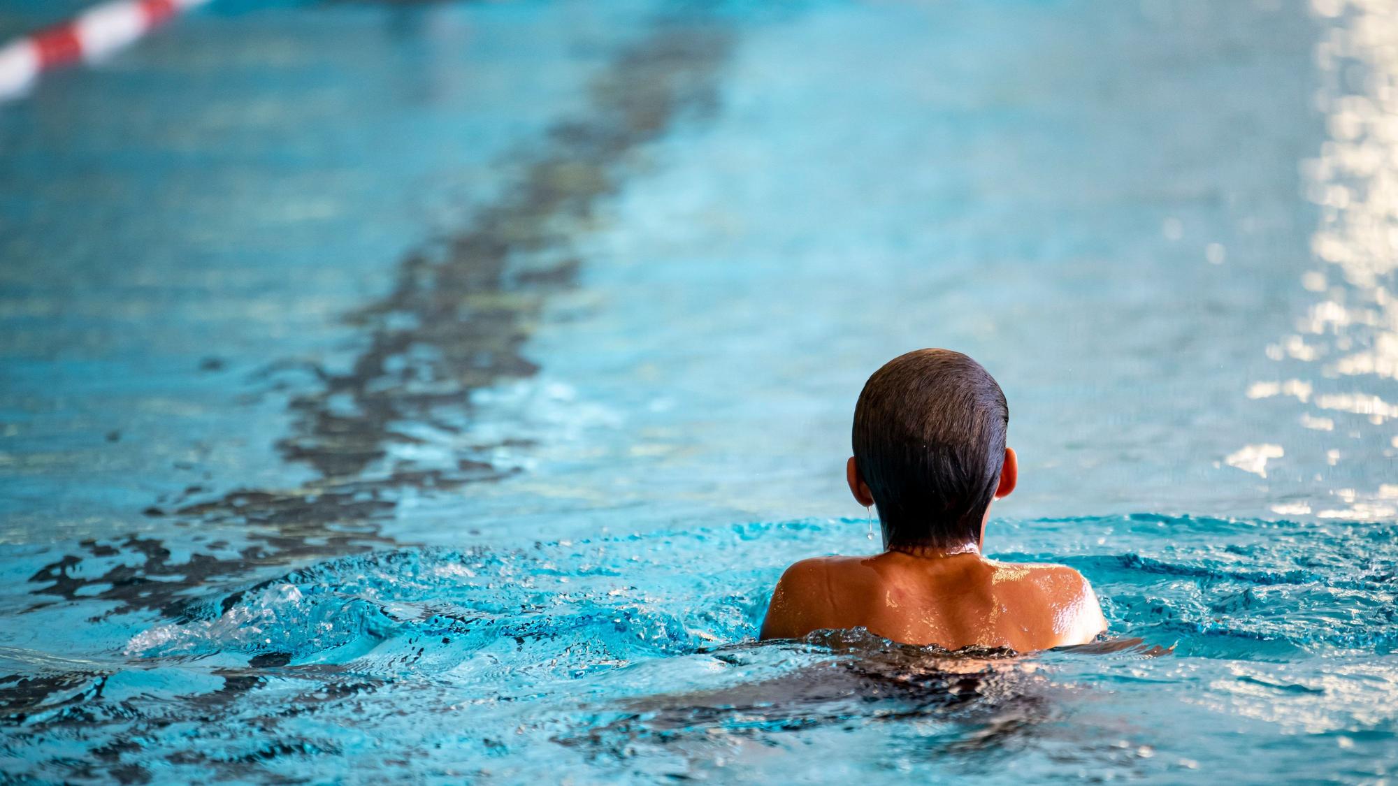 Eine Person, die von Hinten zu sehen ist, schwimmt in einem Hallenbecken.