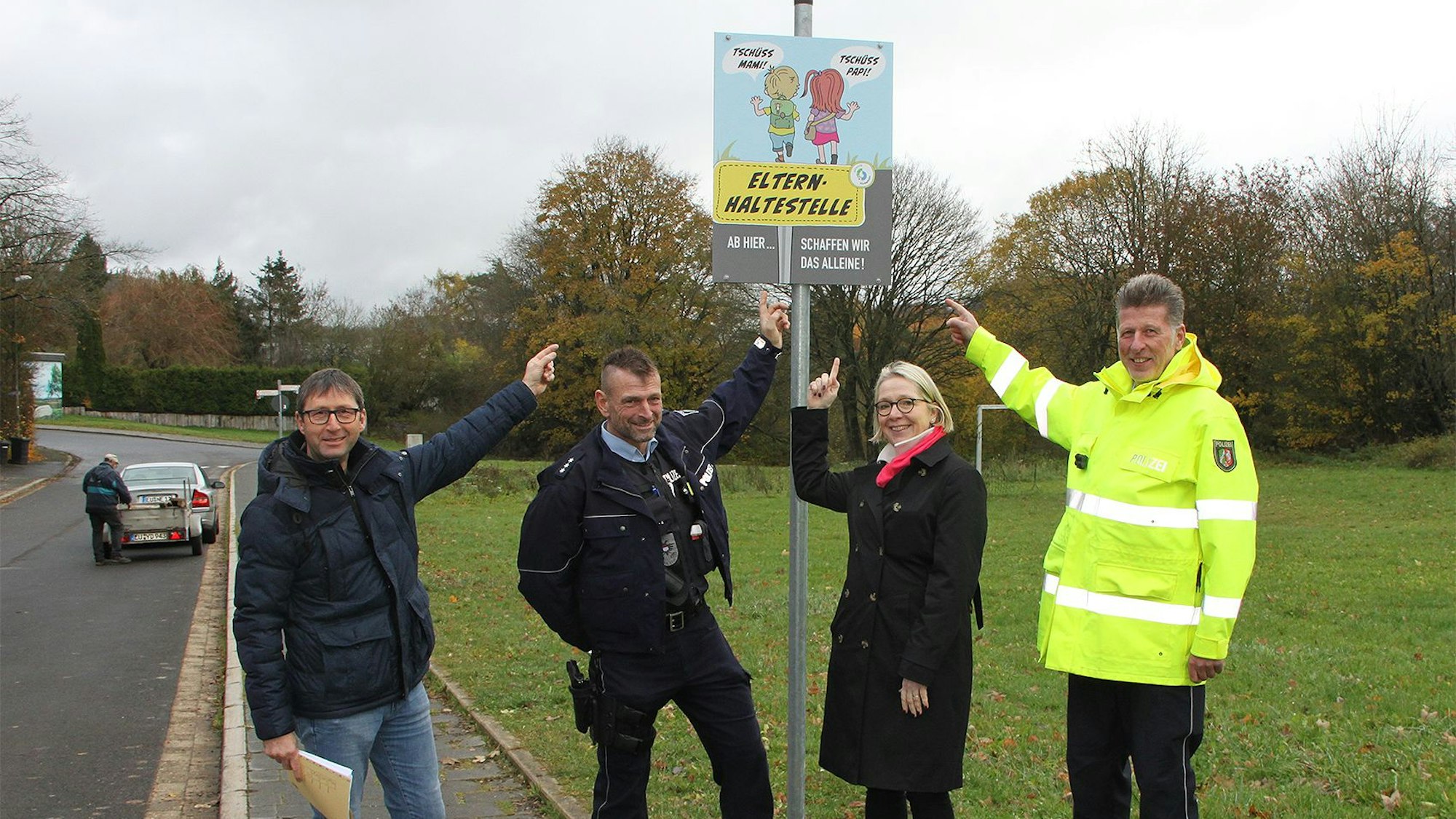 Ordnungsamtsleiter Ferdi Hoss, Schulleiterin Kirsten Schäfer sowie Thomas Claßen und Bernd Schmitz vom Bezirksdienst der Polizei zeigen auf ein Schild mit zwei Schulkindern und der Aufschrift Elternhaltestelle.