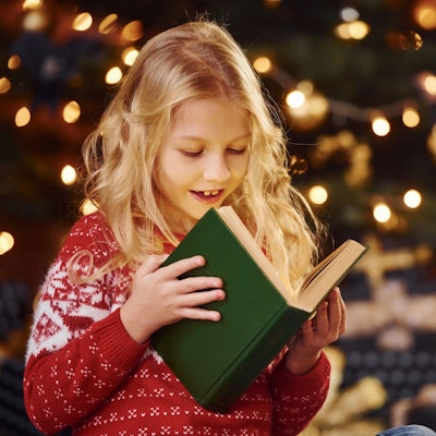Symbolbild: Mädchen liest ein Buch vor weihnachtlicher Beleuchtung