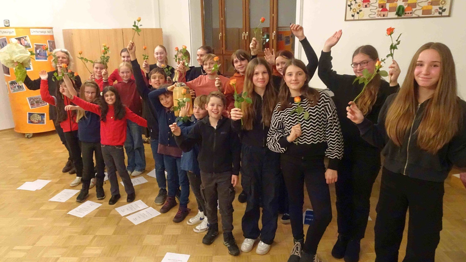 Mehrere Jungen und Mädchen stehen nebeneinander und winken. Jedes Kind hält eine Rose in der Hand.