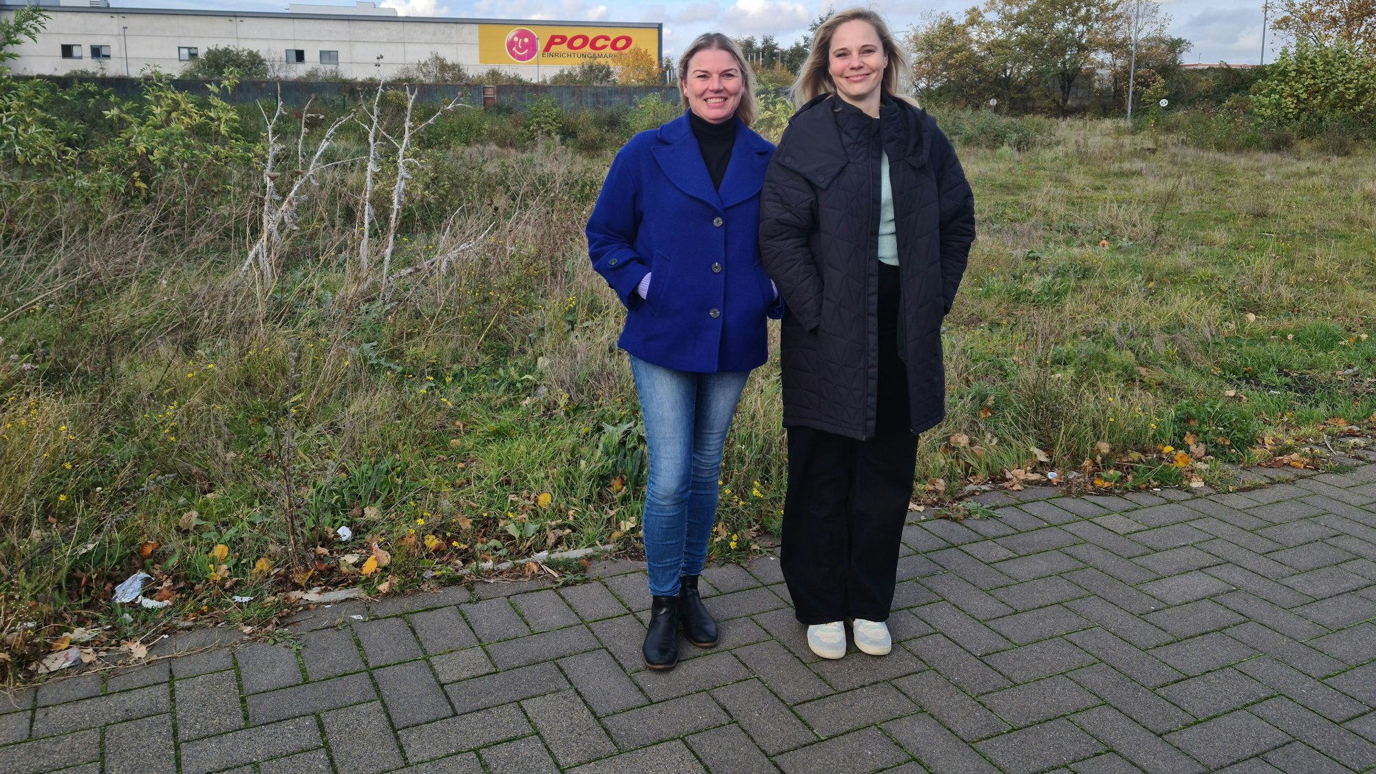 Zwei Frauen stehen vor einer Wiese, im Hintergrund ist der Poco-Markt zu erkennen.