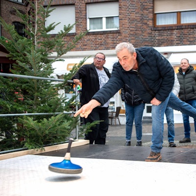 Das Bild zeigt einen Mann, der gerade einen Eisstock auf die Reise schickt. Eine Gruppe schaut ihm dabei zu.