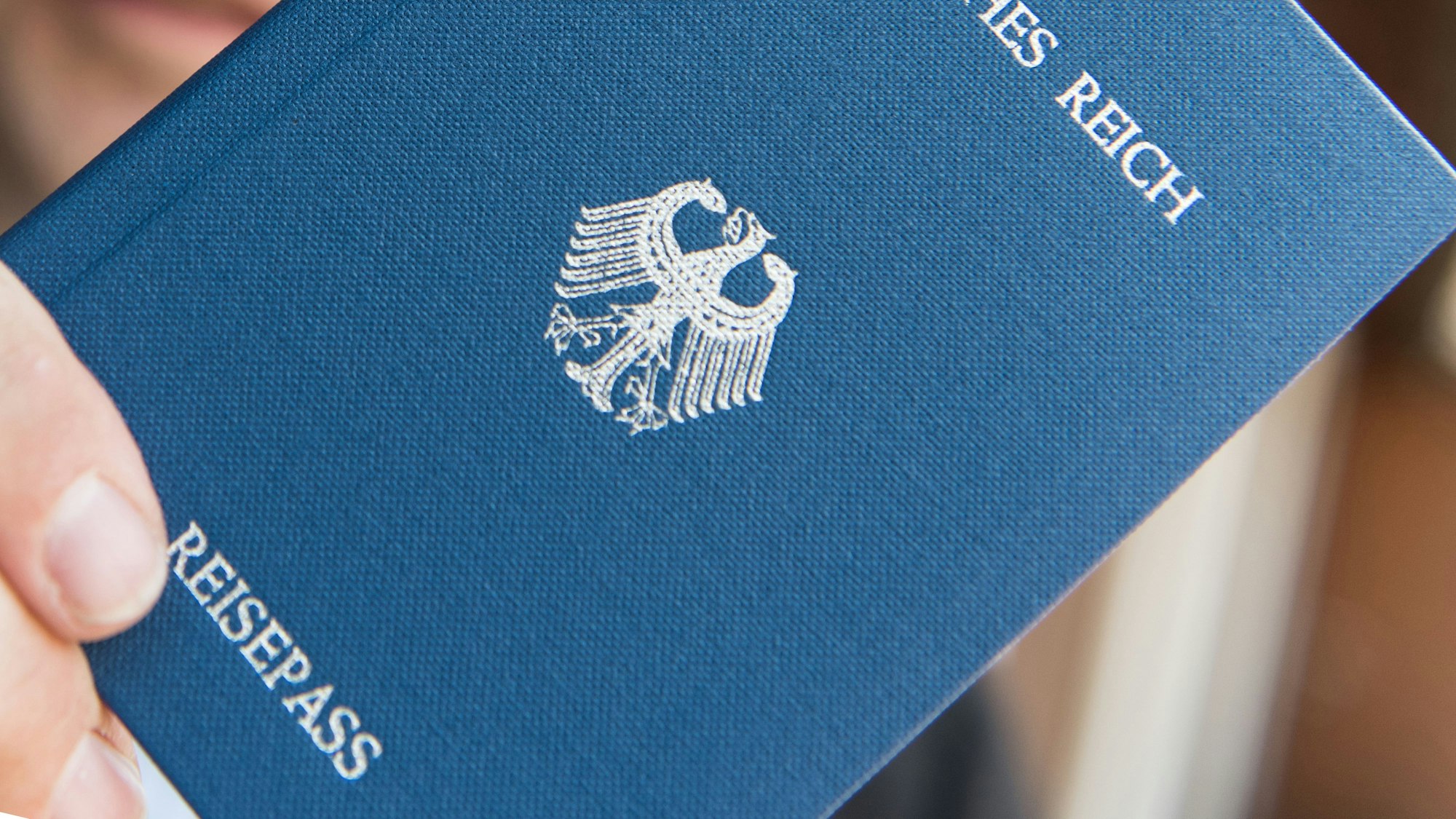 Ein Mann hält ein Heft mit dem Aufdruck «Deutsches Reich Reisepass» in der Hand.