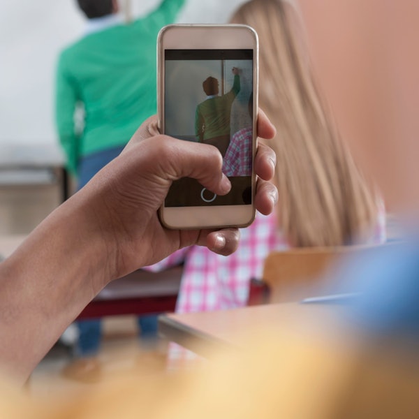 Ein Schüler macht ein Bild vom Lehrer, der etwas an die Tafel schreibt.