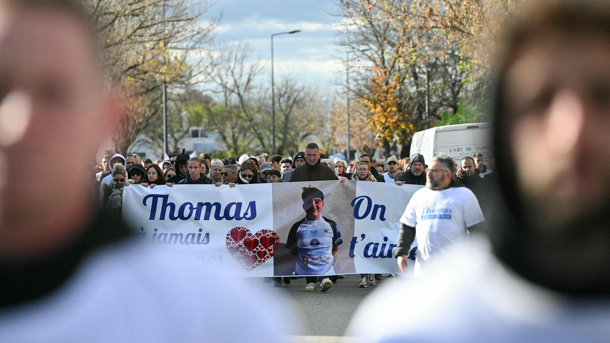Menschen versammeln sich zu einem Trauermarsch und halten ein Banner mit einem Bild des verstorbenen Jugendlichen.