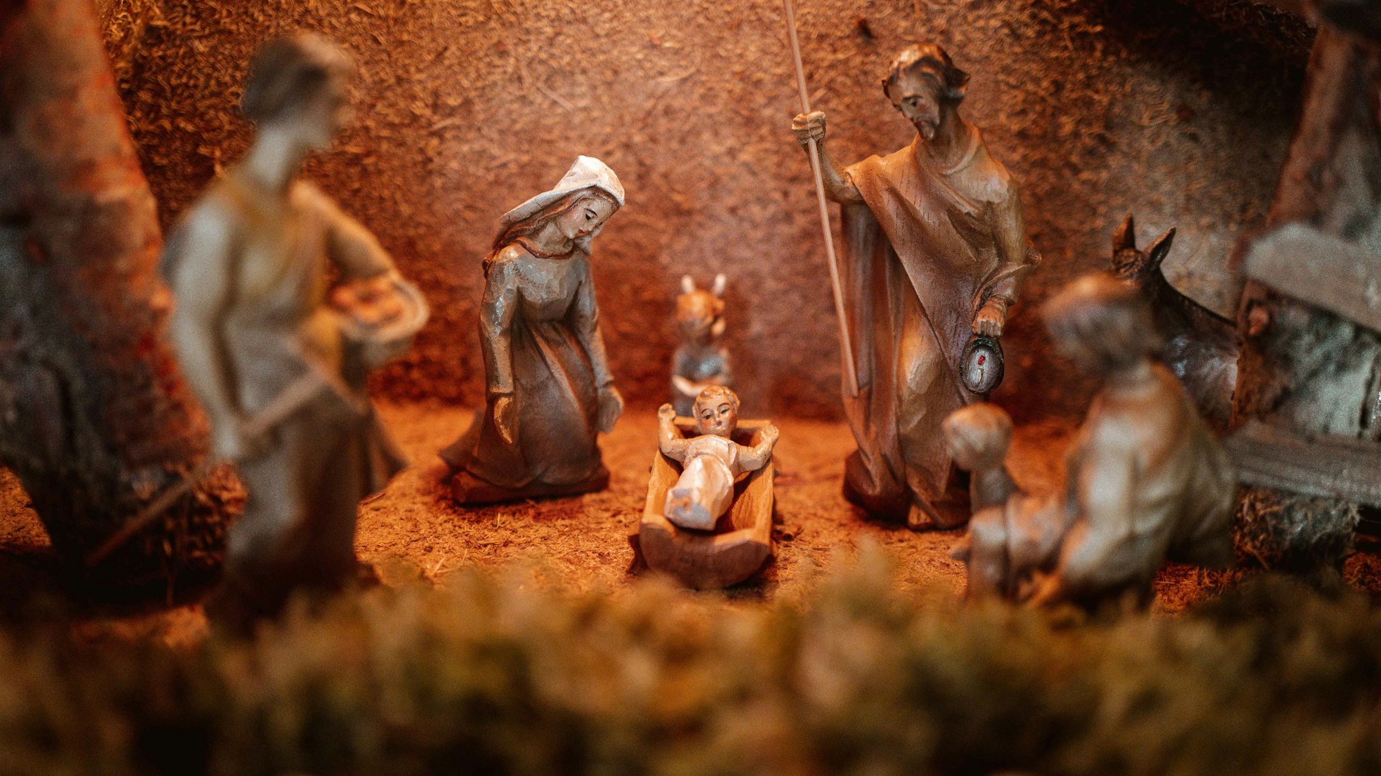 Das Bild zeigt eine Krippe. Links kniet die Figur der Maria, rechts steht Joseph mit einem Stab und in der Mitte liegt das Jesuskind in einer Krippe.