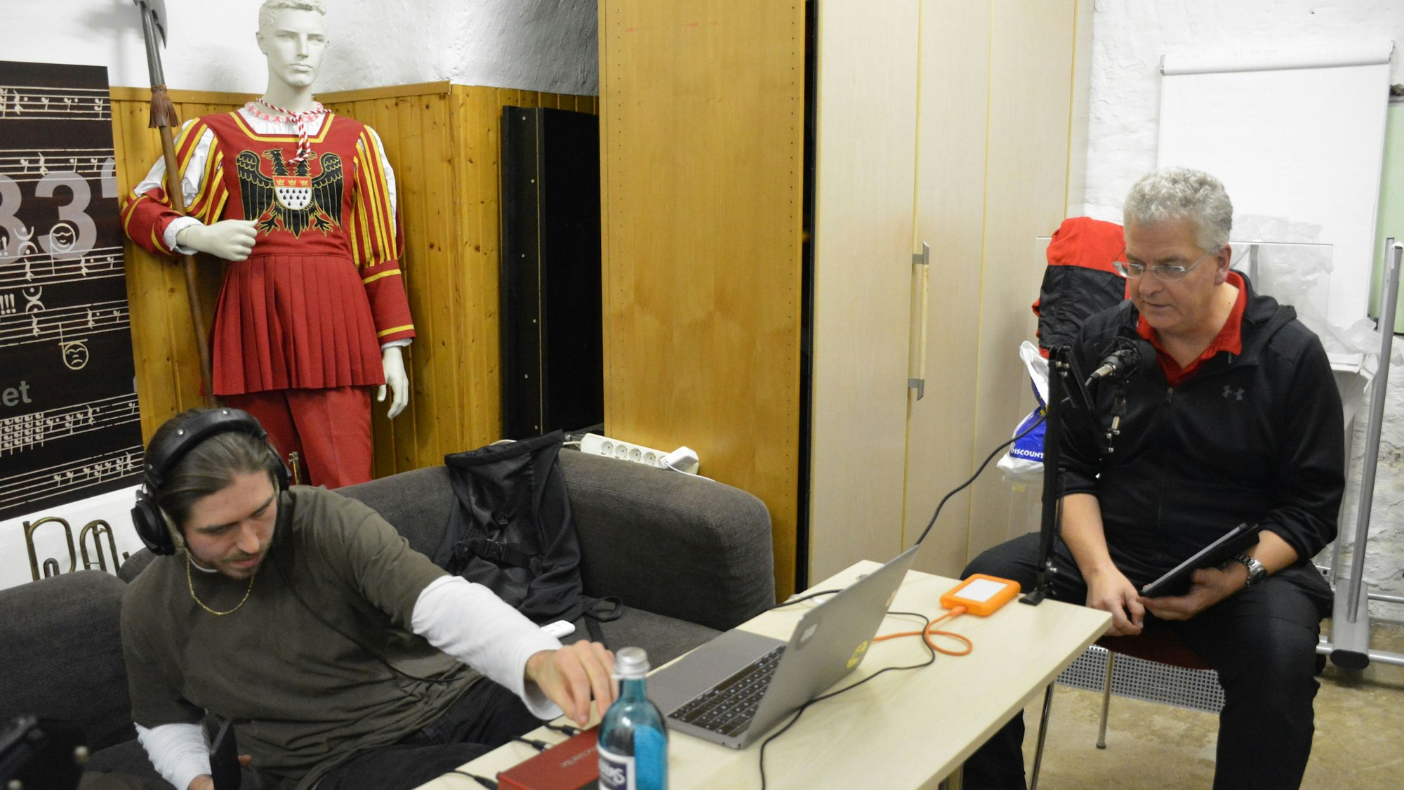 Ein Mann am Mischpult, ein weiterer hält ein Mikrofon.