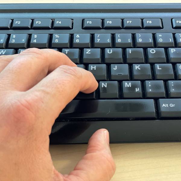 Das Bild zeigt eine Computertastatur und die Finger einer linken Hand.
