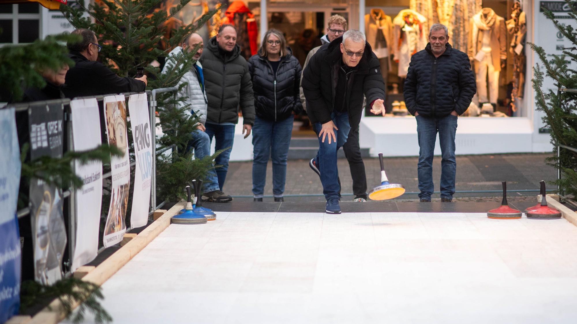Das Bild zeigt eine Gruppe an der Eisstockbahn. Ein Mann hat gerade einen Eisstock geworfen.