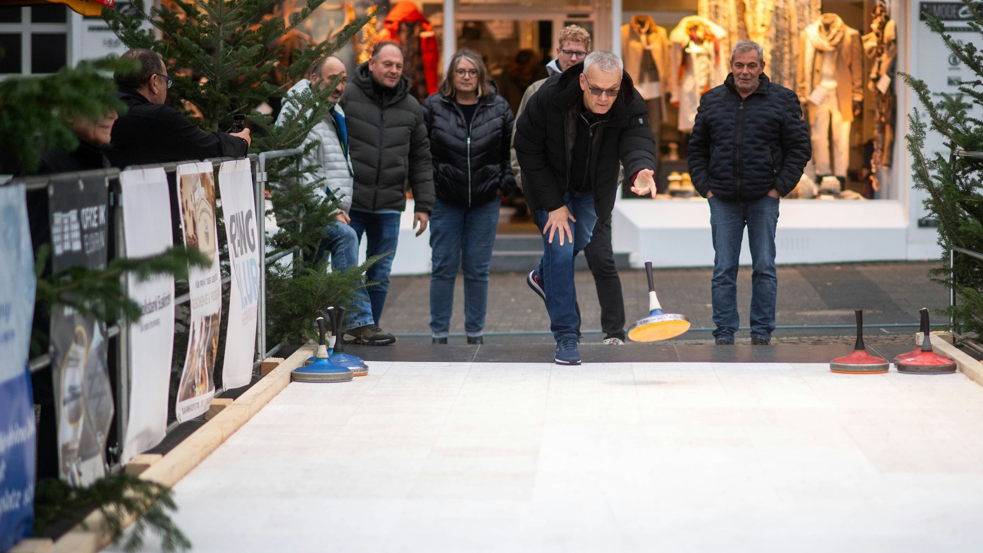 Das Bild zeigt eine Gruppe an der Eisstockbahn. Ein Mann hat gerade einen Eisstock geworfen.