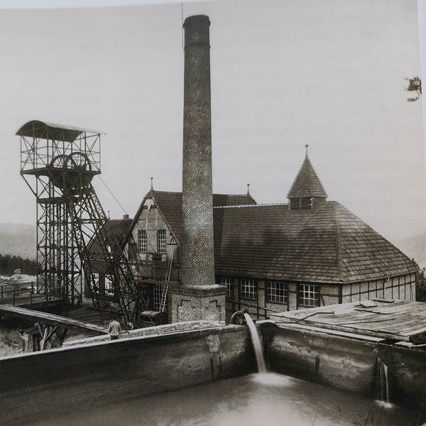 Historische Aufnahme einer alten Grubenanlage mit Förderturm und Schornstein, davor Halden.