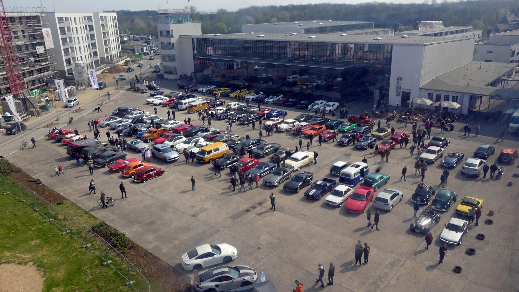 Auf einem Parkplatz stehen einige Autos vor einem großen zweistöckigen Gebäude.