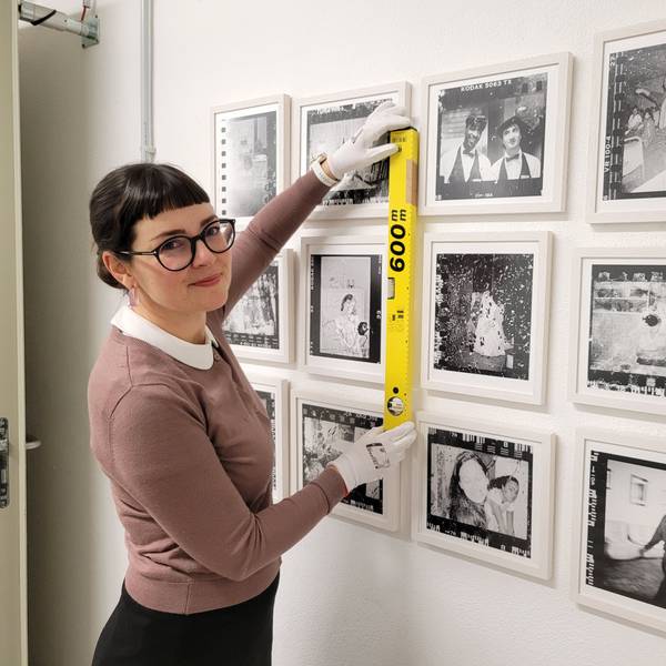 Eine dunkelhaarige Frau hängt Fotos für eine Ausstellung auf.