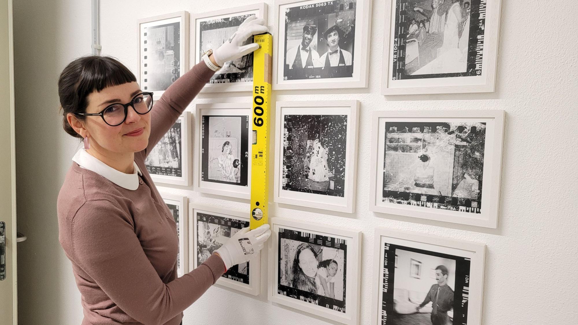 Eine dunkelhaarige Frau hängt Fotos für eine Ausstellung auf.