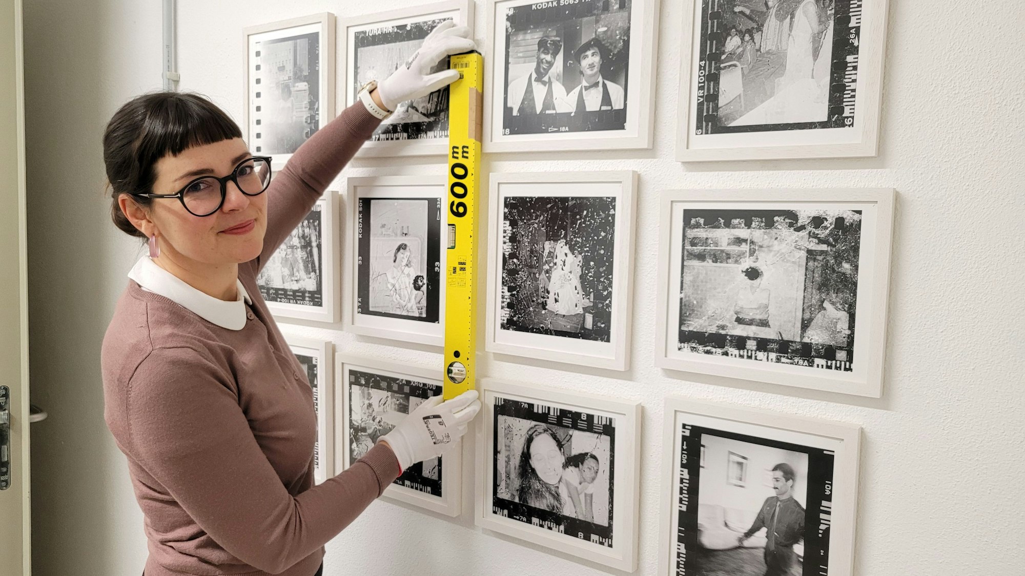 Zu sehen ist eine Frau, die mit einer Wasserwaage kontrolliert, ob die Fotografien richtig hängen.