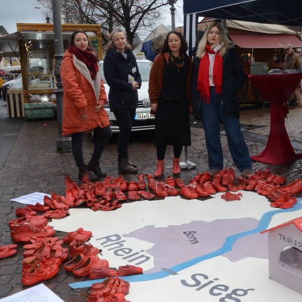 Vier Frauen; sie haben aus roten Schuhen die Umrisse des Rhein-Sieg-Kreises ausgelegt. Im Vordergrund steht ein symbolisches Frauenhaus mit der Aufschrift 30 Betten.