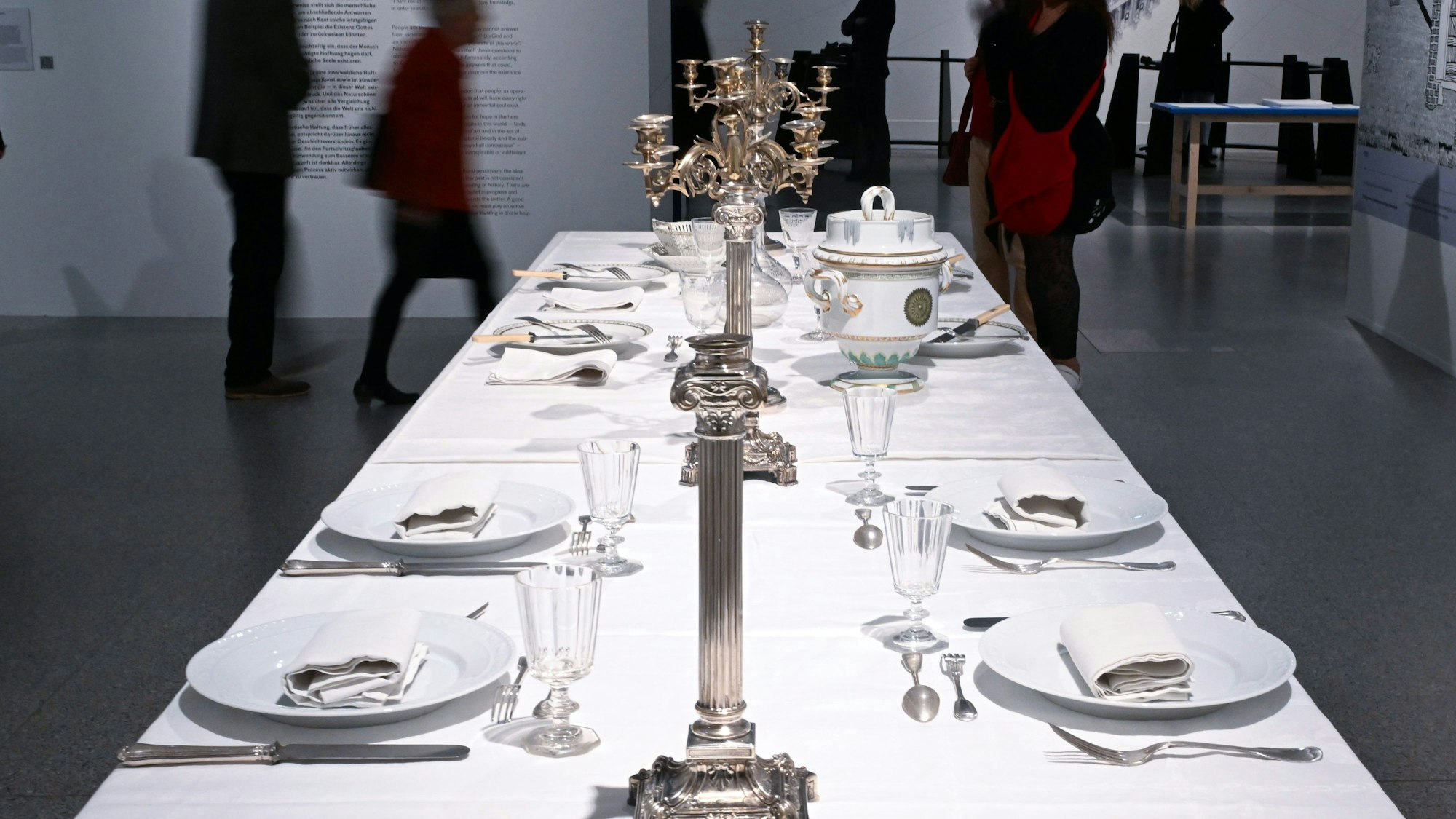Besucher gehen in der Ausstellung an einem gedeckten Tisch vorbei.
