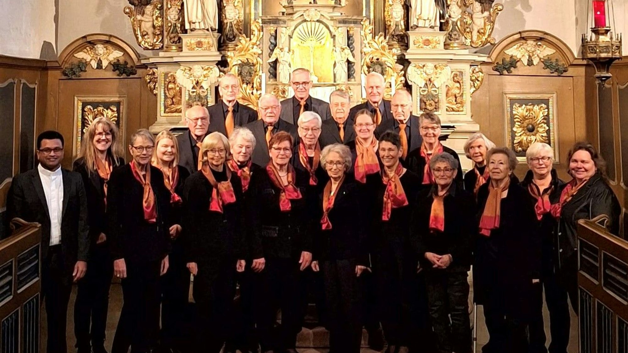 Frauen und Männer stehen gemeinsam in dunkler Kleidung mit roten Schals vor dem Altar der Kirche in Marienheide.