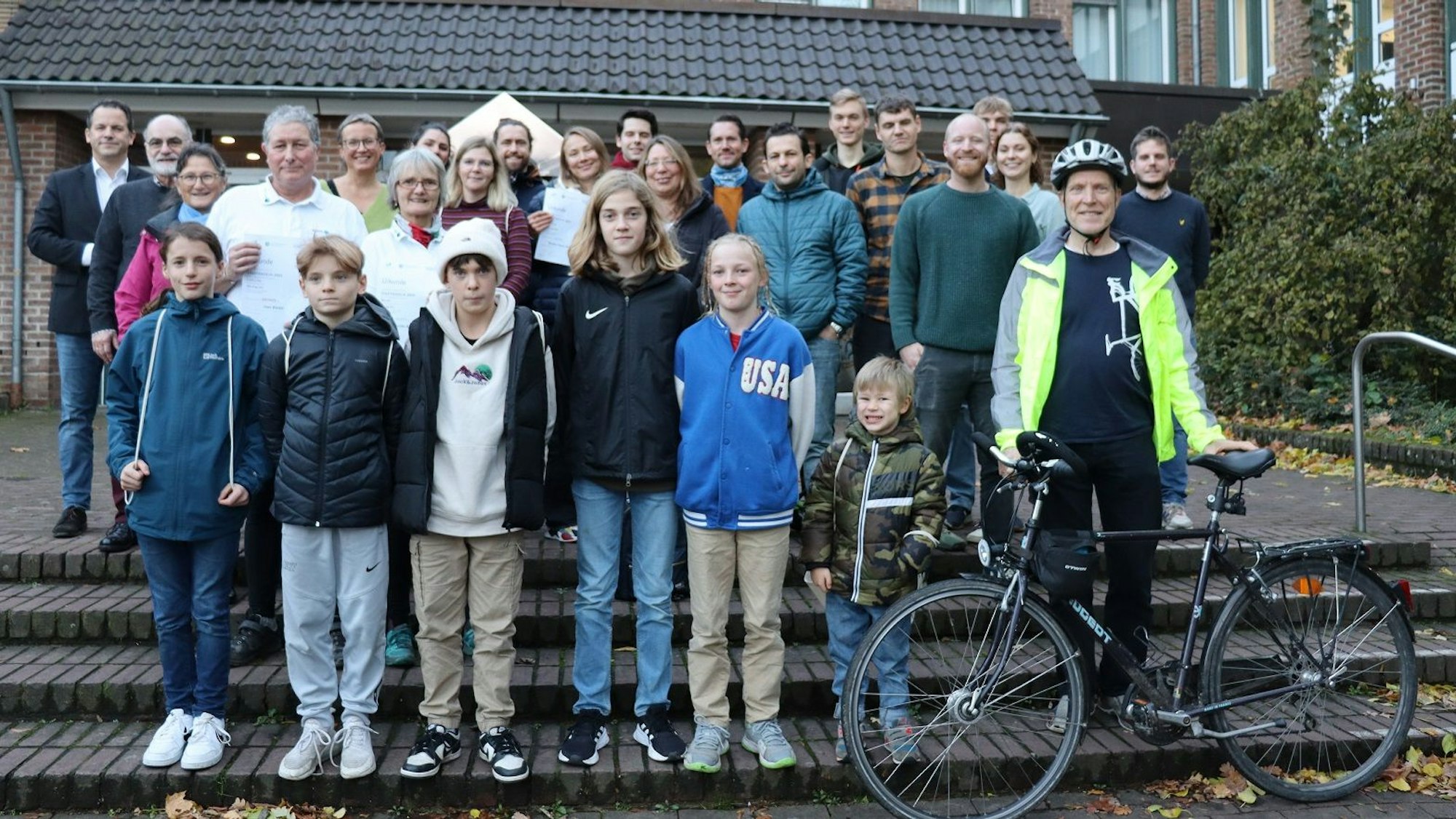 Eine Gruppe von Radfahrerinnen und Radfahrern mit einem Fahrrad auf den Stufen vor dem Rathaus.