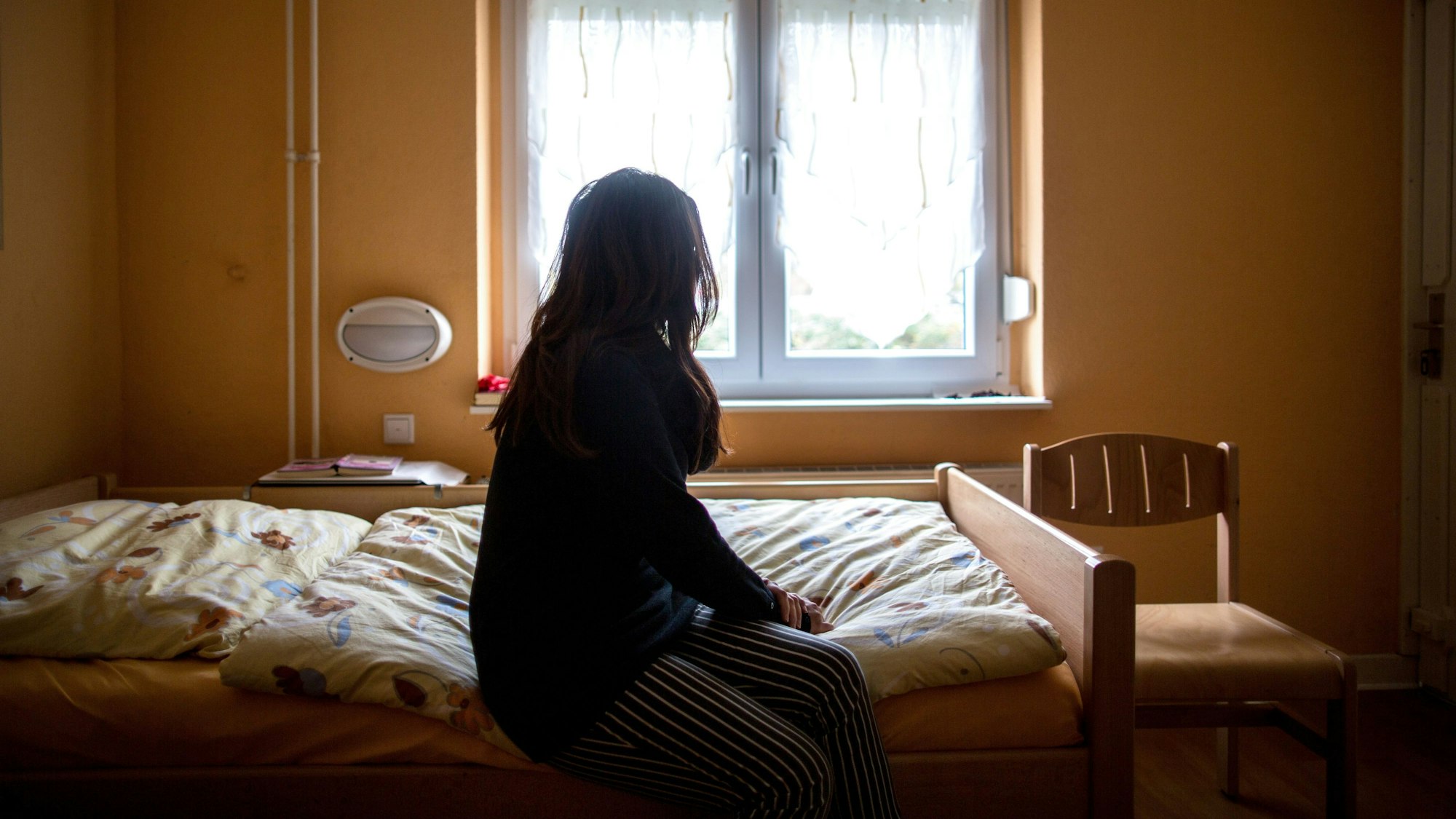 Eine Frau sitzt in einem Frauenhaus auf einem Bett.