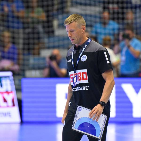 VfL-Trainer Gudjon Valur Sigurdsson läuft mit einer Zeigetafel über ein Handball-Spielfeld.