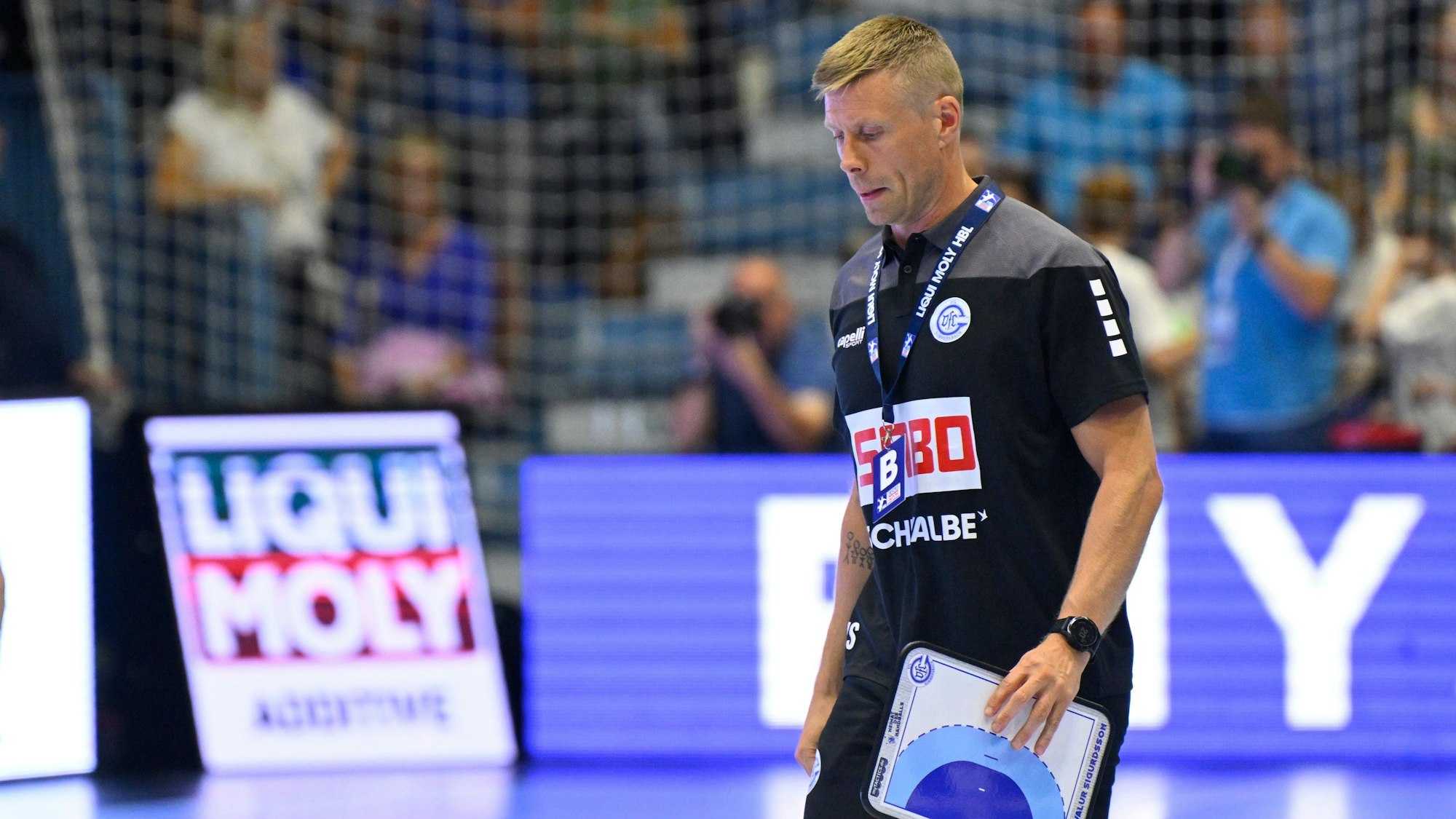 VfL-Trainer Gudjon Valur Sigurdsson läuft mit einer Zeigetafel über ein Handball-Spielfeld.