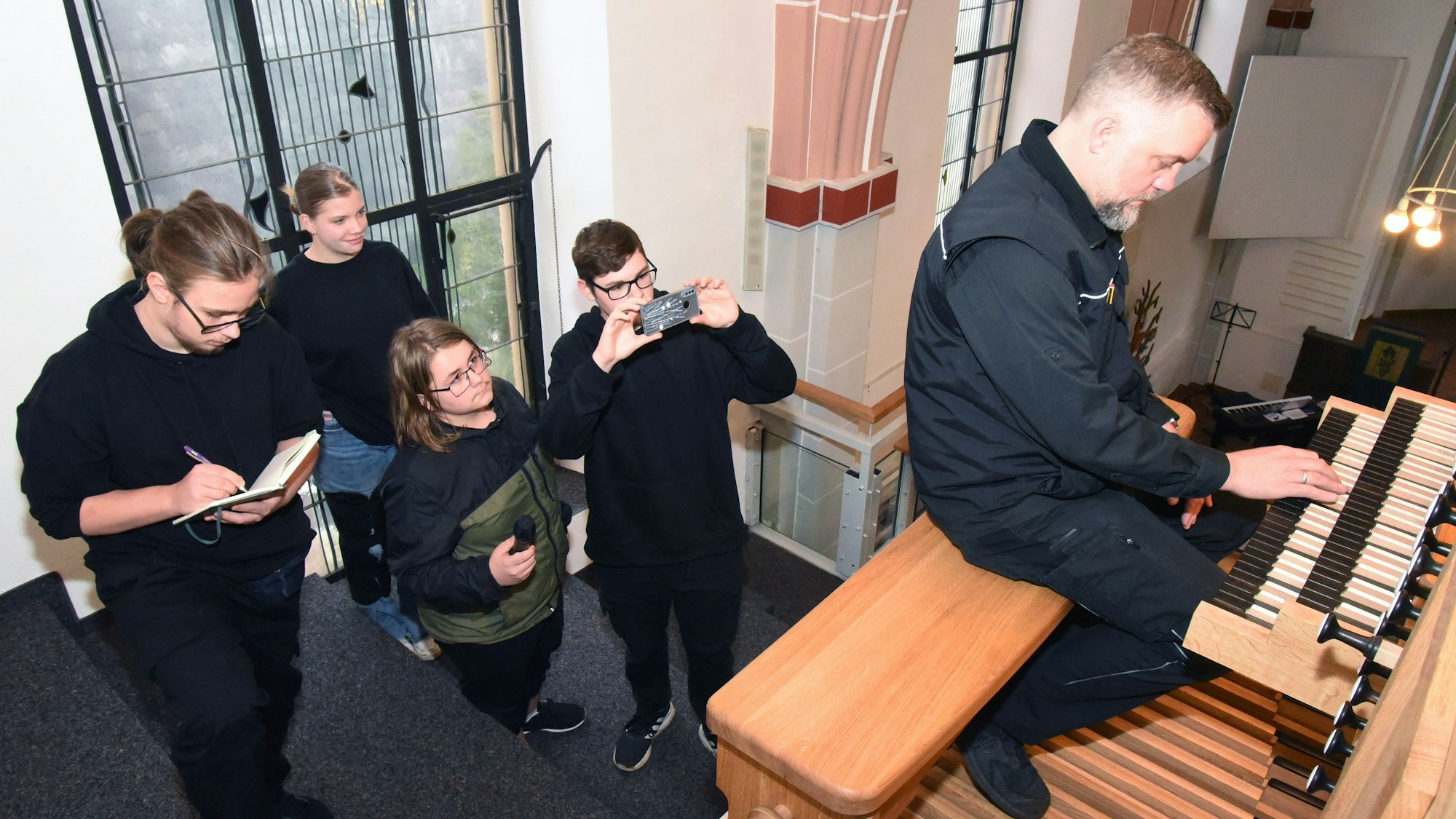 Mehrere Jugendliche filmen, wie ein Mann an einer Orgel sitzt und spielt.