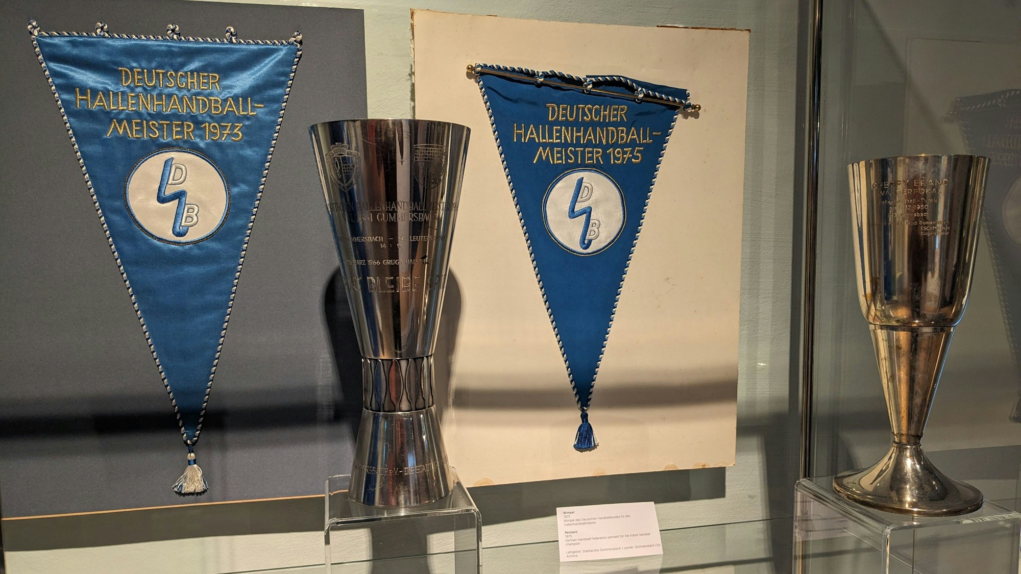 Bild von zwei Pokalen und zwei Wimpeln in einer Glasvitrine.