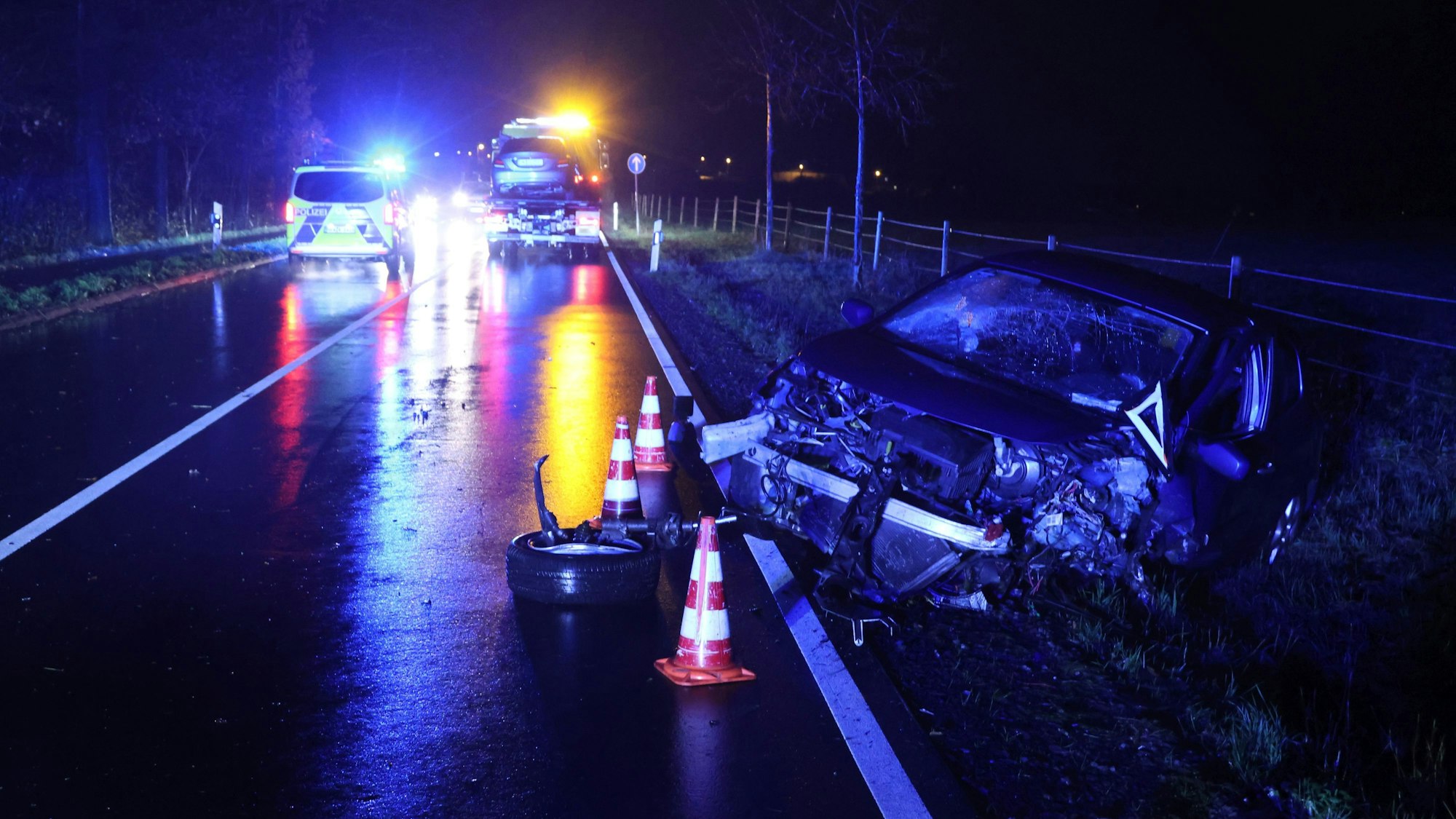 Ein Auto mit zertrümmerter Front steht am Rand einer nächtlich beleuchteten Straße.
