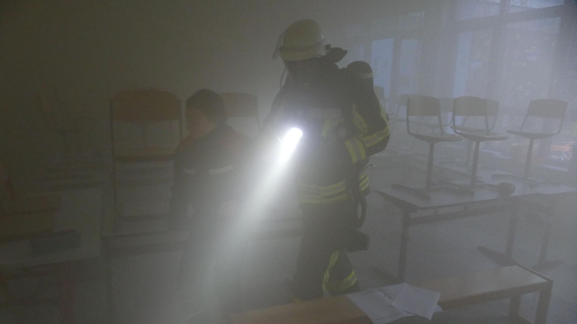 Fast null ist die Sicht, als dieser Feuerwehrmann ein Mädchen aus dem vernebelten Klassenzimmer führt.