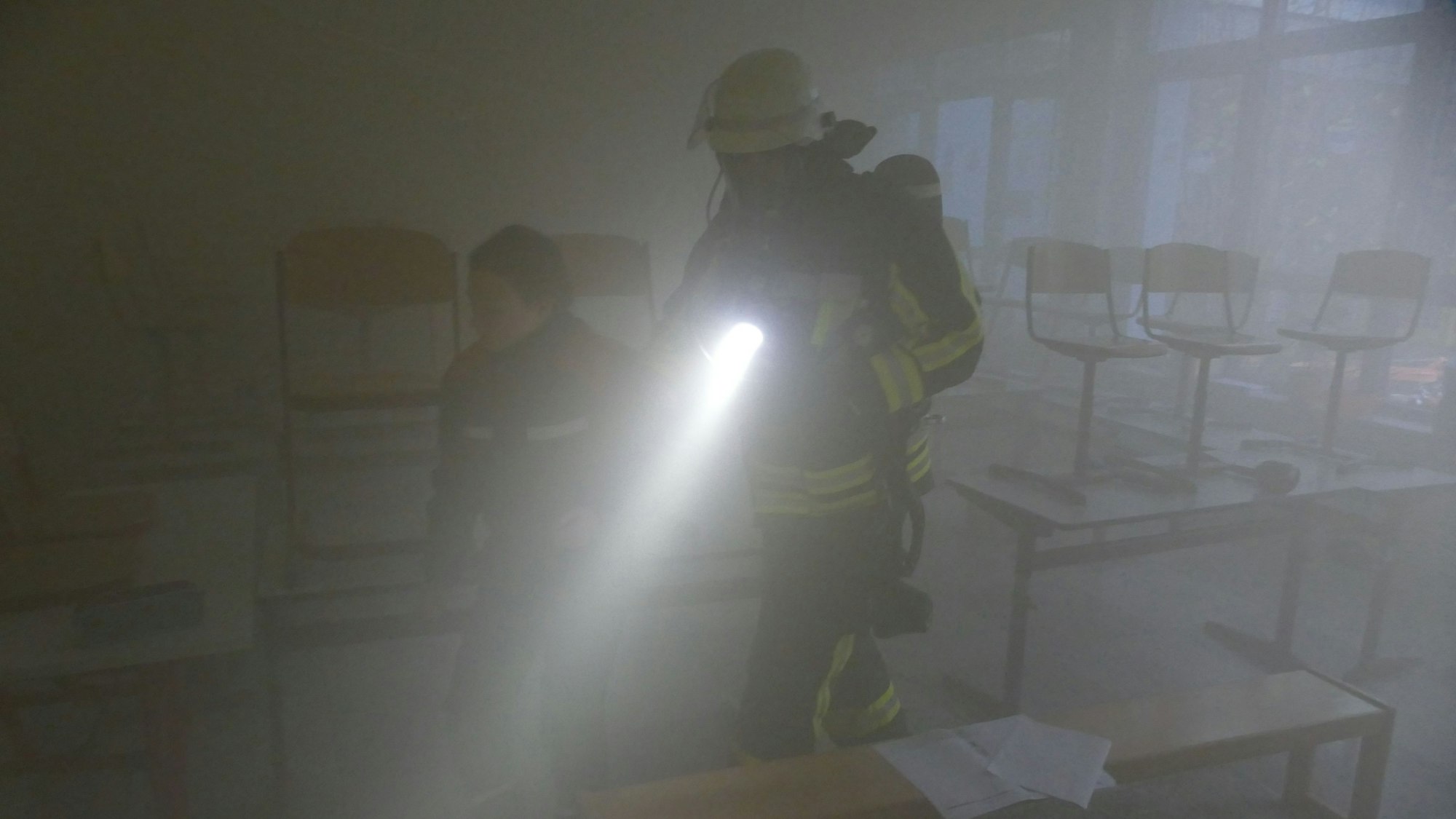 Fast null ist die Sicht, als dieser Feuerwehrmann ein Mädchen aus dem vernebelten Klassenzimmer führt.