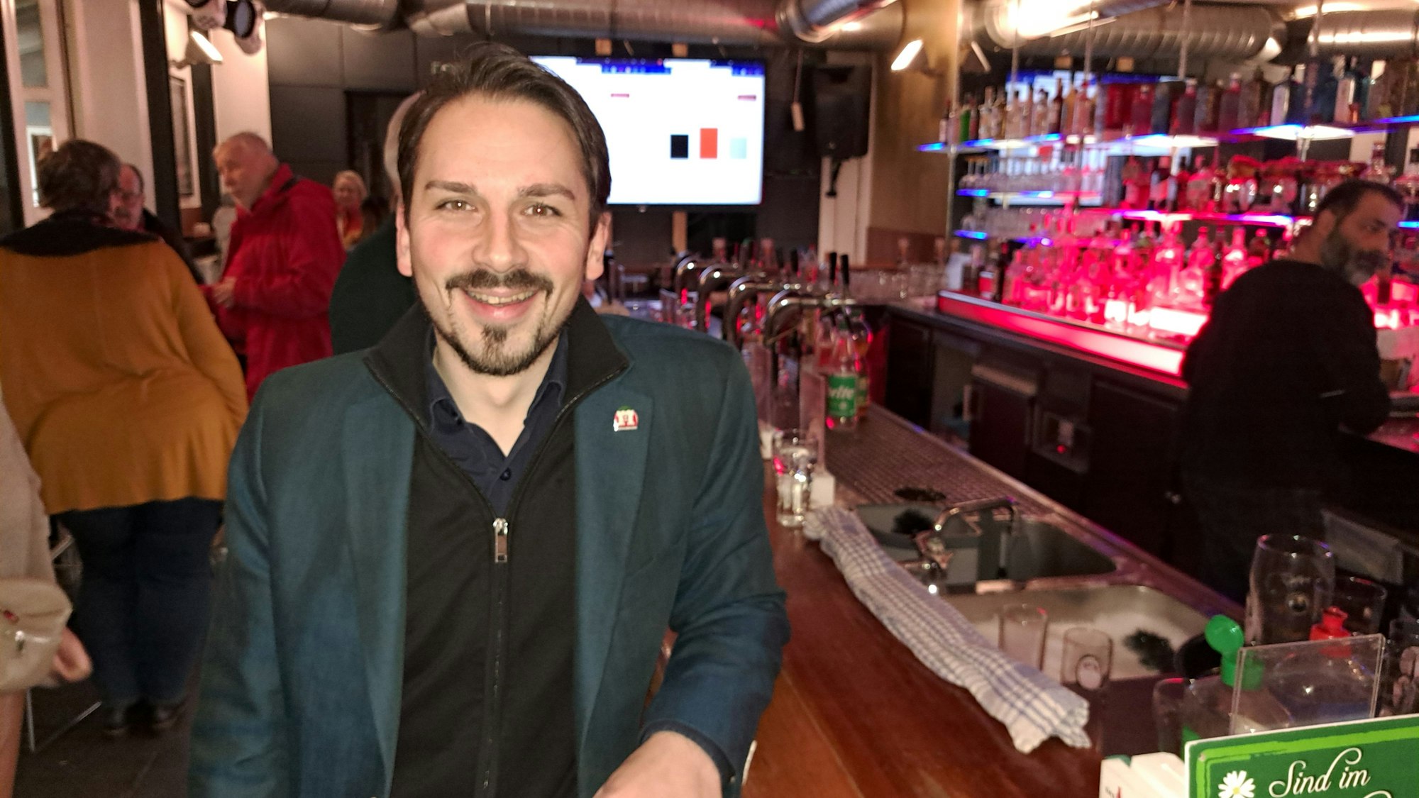 Matthias Großgarten (SPD), ein junger Mann mit dunklem Bart, steht an einer Theke in Niederkassel.